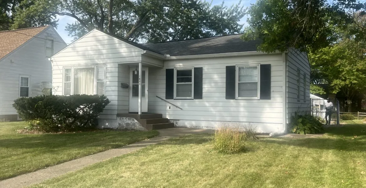 Single-story residential house with white siding, green shutters, and a front walkway.
